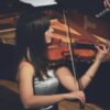 woman playing violin beside grand piano