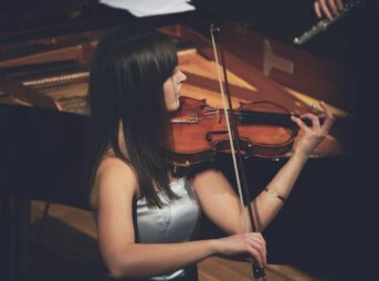 woman playing violin beside grand piano